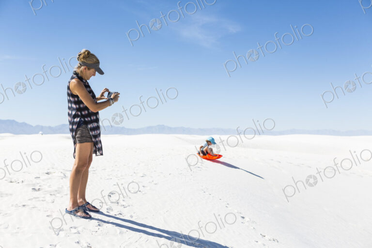 Mother taking picture of son sledding on sand dunes