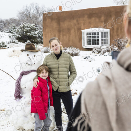 Mother taking portrait of her children with snowman in background Mother taking portrait of her children with snowman in background