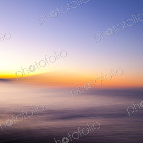 Motion blurred beach at sunset, a red glow on the horizon.