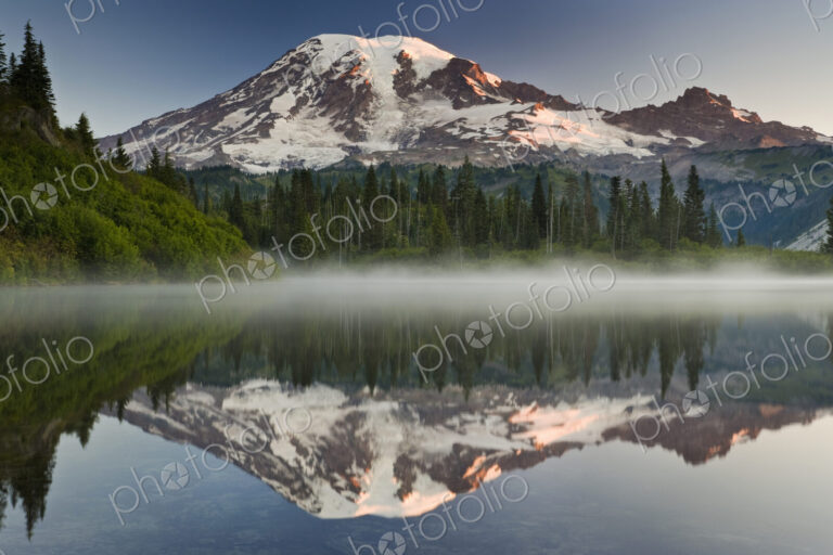 Mount Rainier, a snow capped peak, surrounded by forest reflected in one of many lakes…