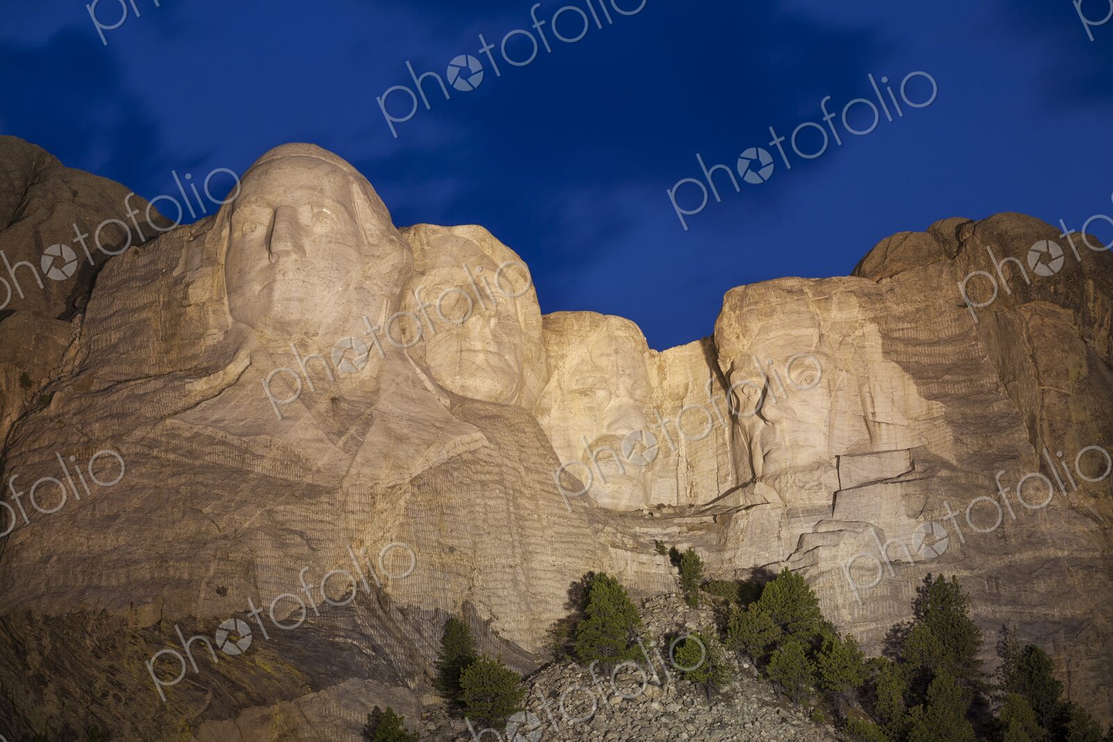 Mount Rushmore illuminated at dusk beneath a deep blue sky with soft cloud motion,…