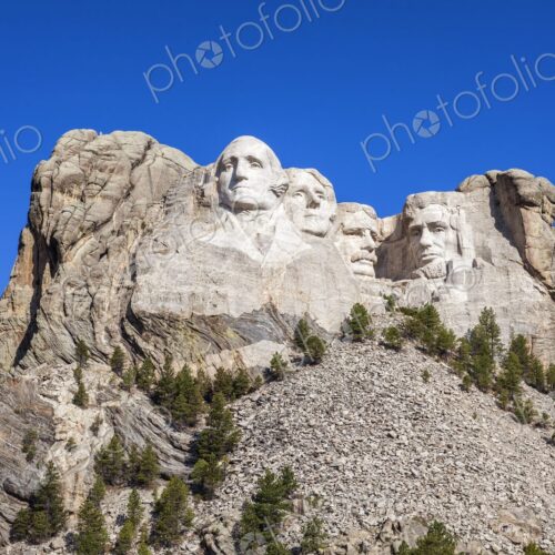 Mount Rushmore with four presidential sculptures carved in granite above pine forest…