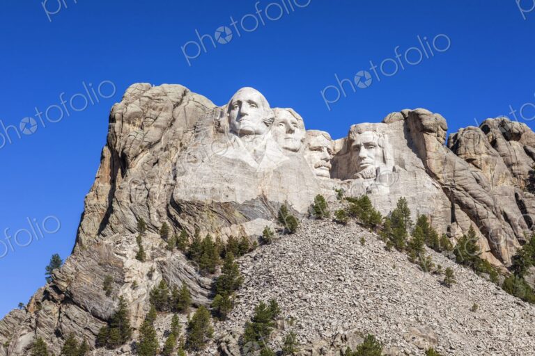 Mount Rushmore with four presidential sculptures carved in granite above pine forest…