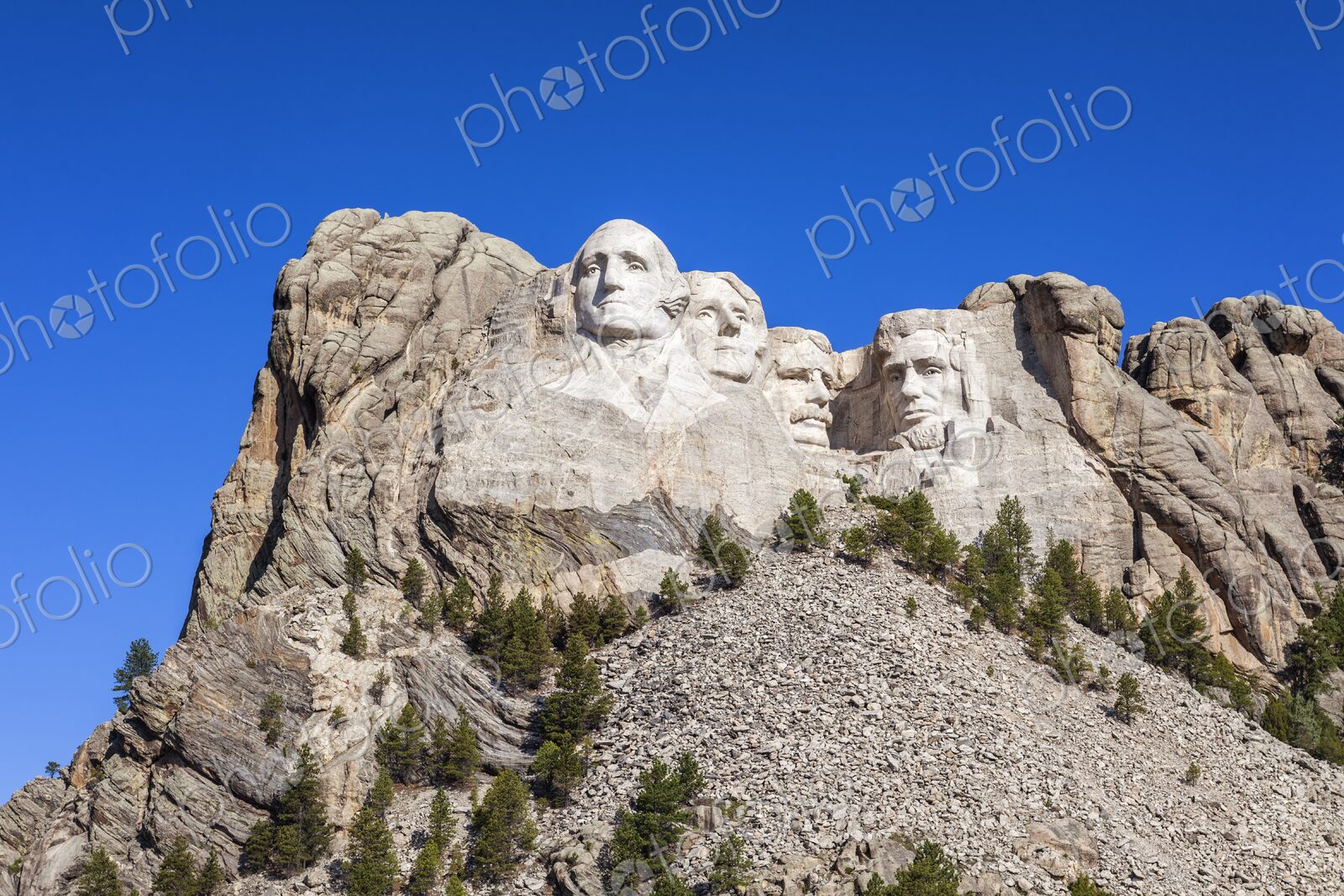 Mount Rushmore with four presidential sculptures carved in granite above pine forest…