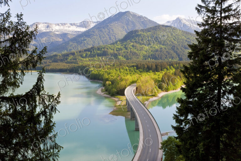 Mountain landscape with forests and bridge crossing dam in the foreground.