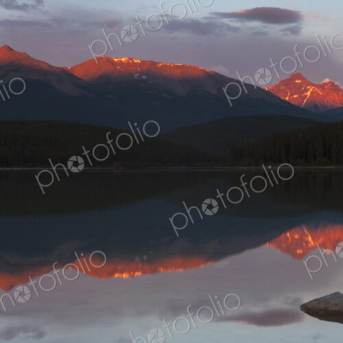 Mountains reflected in a lake and the sun reflecting off the snow covered high slopes.