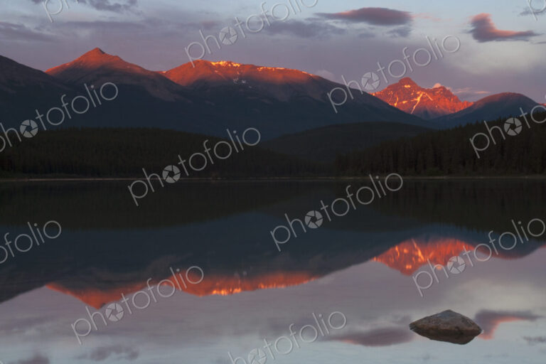 Mountains reflected in a lake and the sun reflecting off the snow covered high slopes.