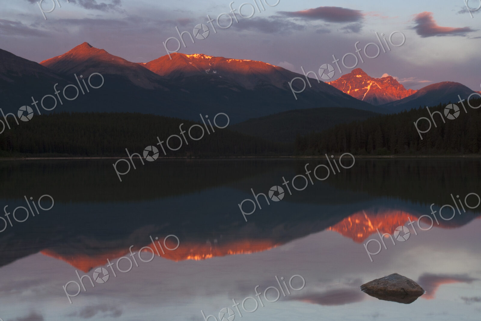 Mountains reflected in a lake and the sun reflecting off the snow covered high slopes.