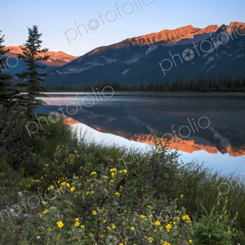 Mountains reflected in a lake and the sun reflecting off the snow covered high slopes.