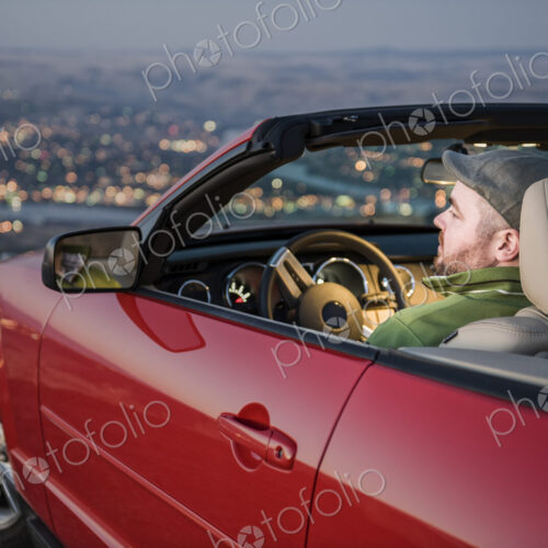 Msn parked in his convertible sports car watching the sunset over a city Msn parked in his convertible sports car watching the sunset over a city