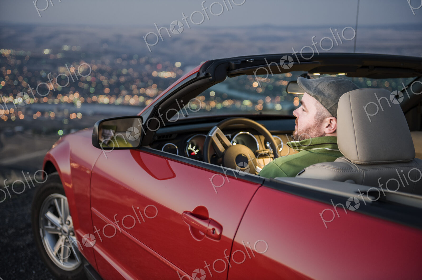 Msn parked in his convertible sports car watching the sunset over a city