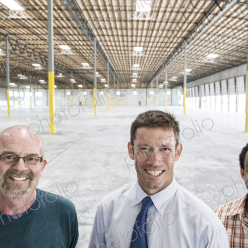 Multi-racial group of men standing in front of loading dock doors in a new empty…