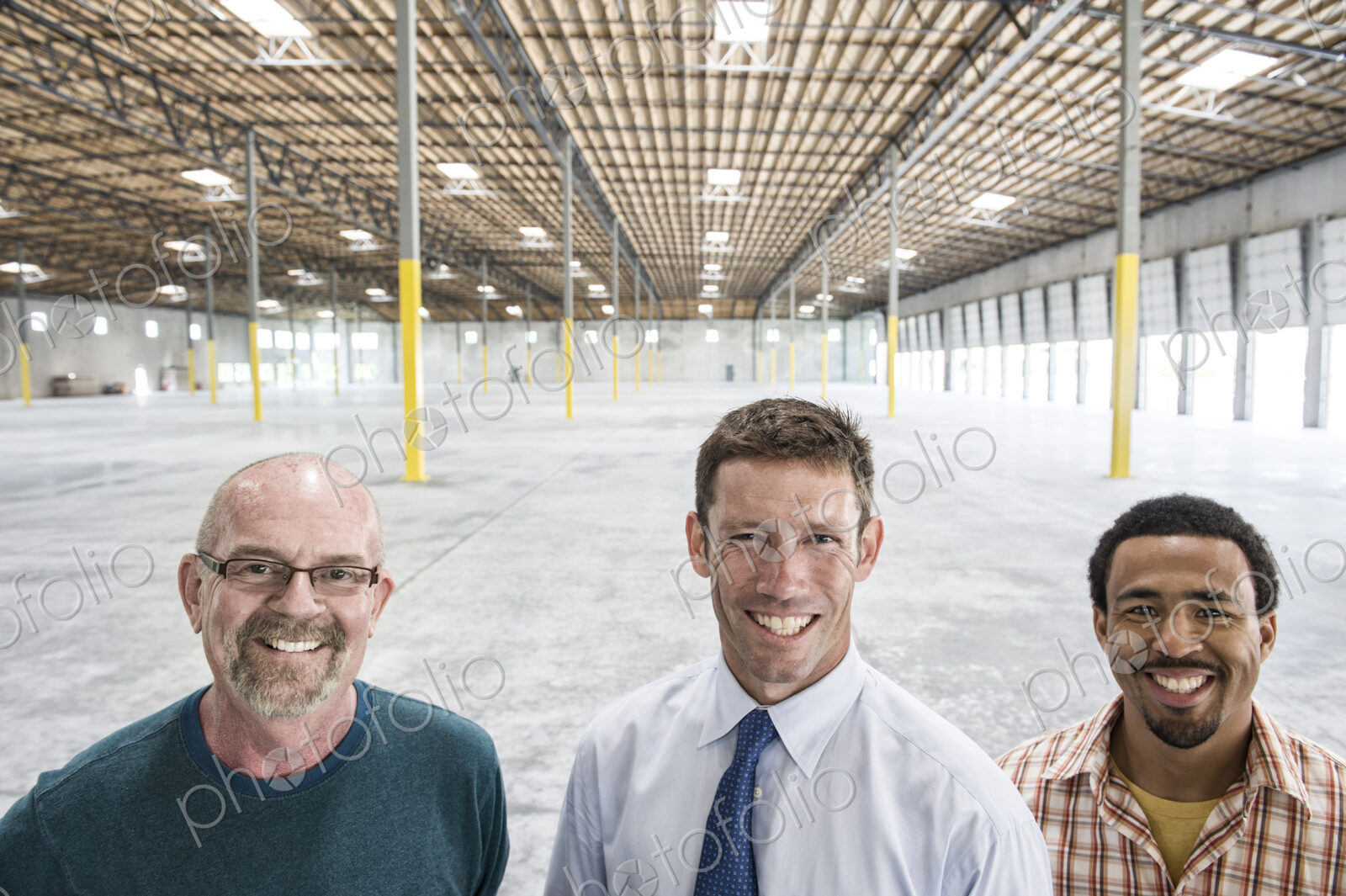 Multi-racial group of men standing in front of loading dock doors in a new empty…