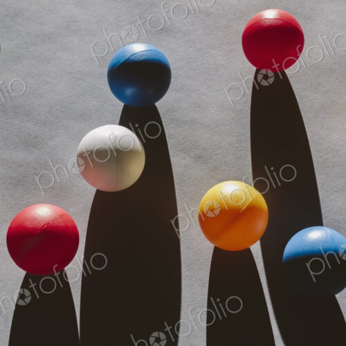 Multicolored balls arranged on wood background, casting long shadows