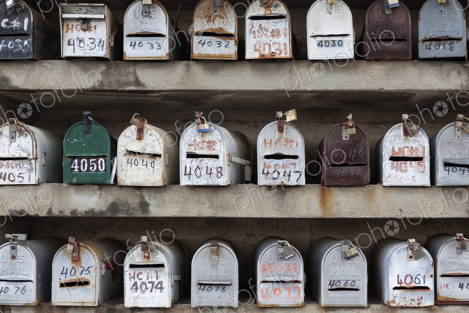 Multiple rows of weathered U.S. Mail mailboxes with hand-painted numbers are mounted…