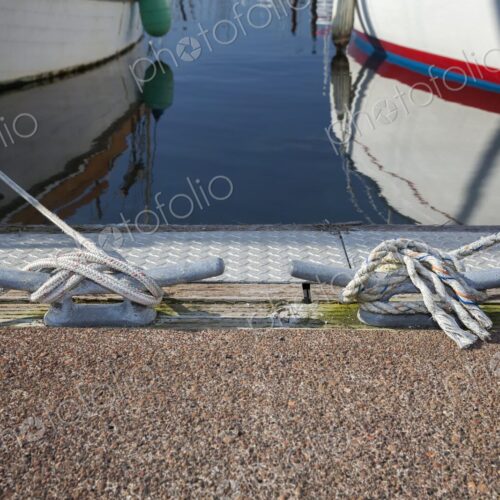 Nautical scene showing two boats moored with ropes secured to dock cleats at… Nautical scene showing two boats moored with ropes secured to dock cleats at…