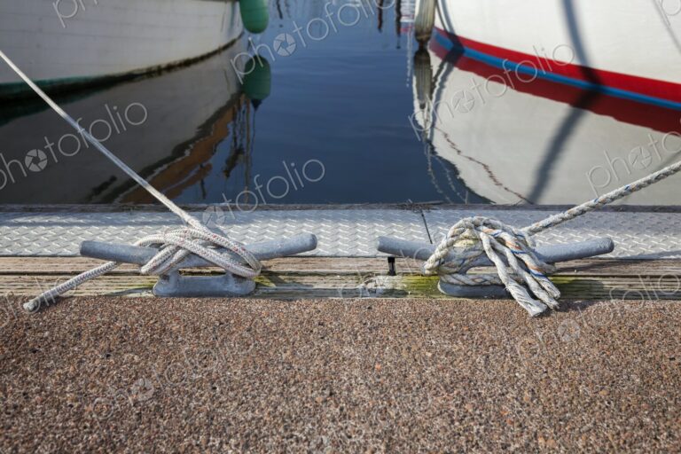 Nautical scene showing two boats moored with ropes secured to dock cleats at…