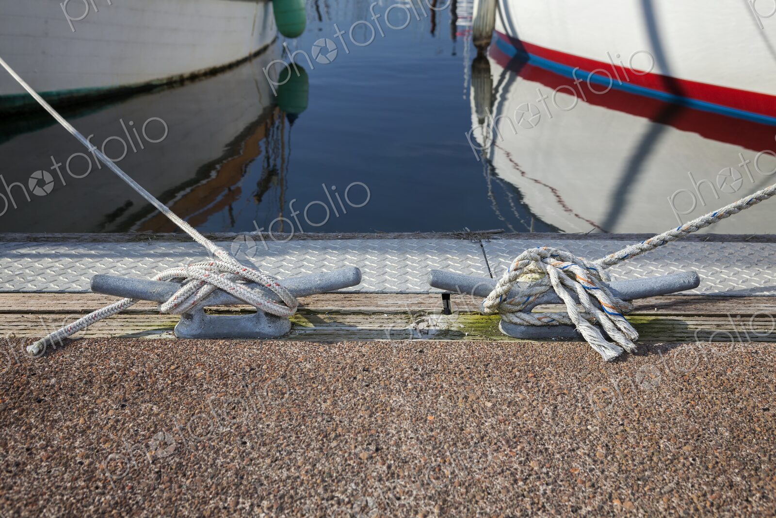 Nautical scene showing two boats moored with ropes secured to dock cleats at…