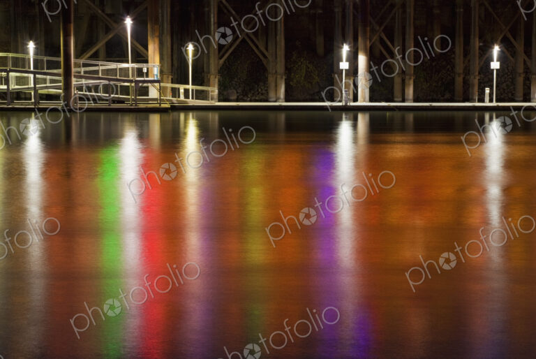 Neon lights reflect off Sacramento River water surface at night, Sacramento