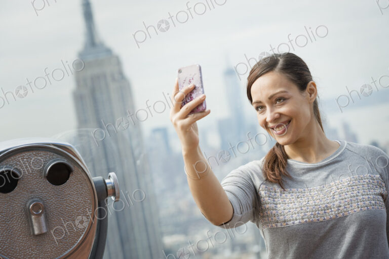 New York City. An observation deck overlooking the Empire State Building. A woman…