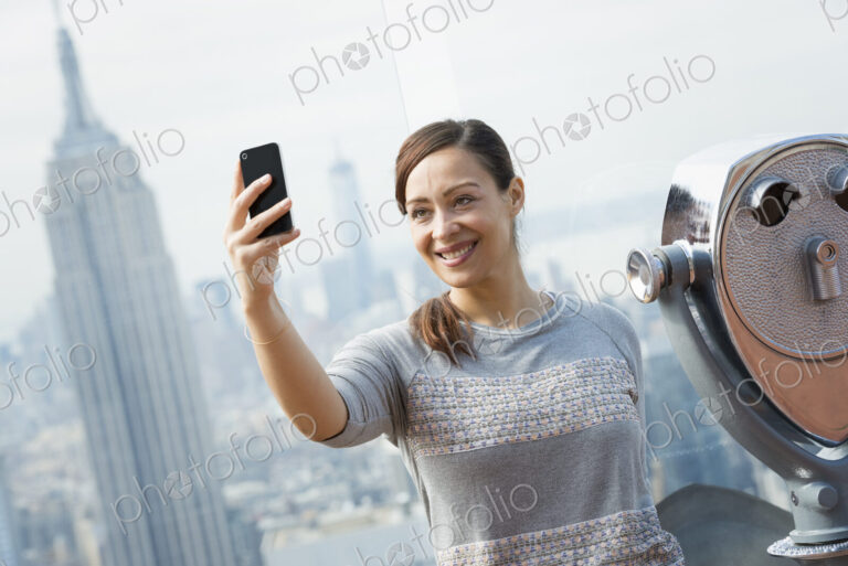 New York City. An observation deck overlooking the Empire State Building. A woman…
