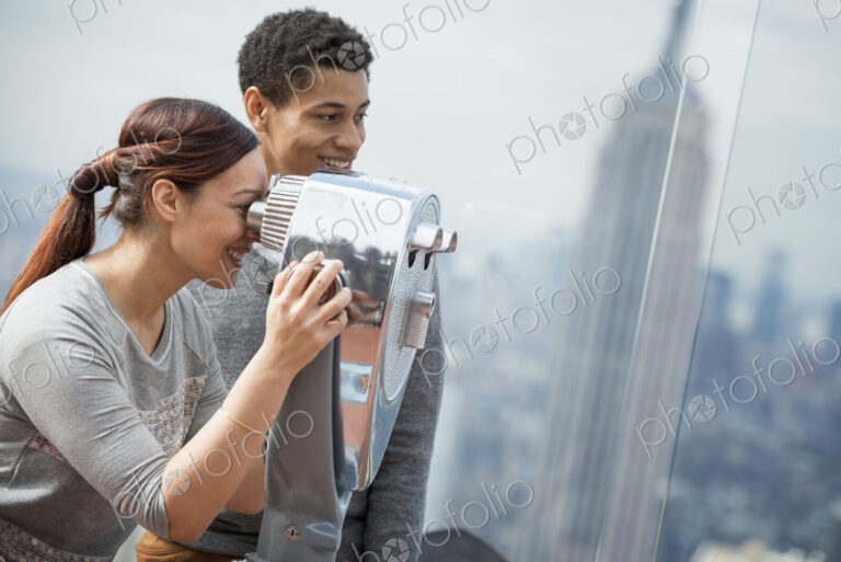 New York City. An observation deck overlooking the Empire State Building. A young…