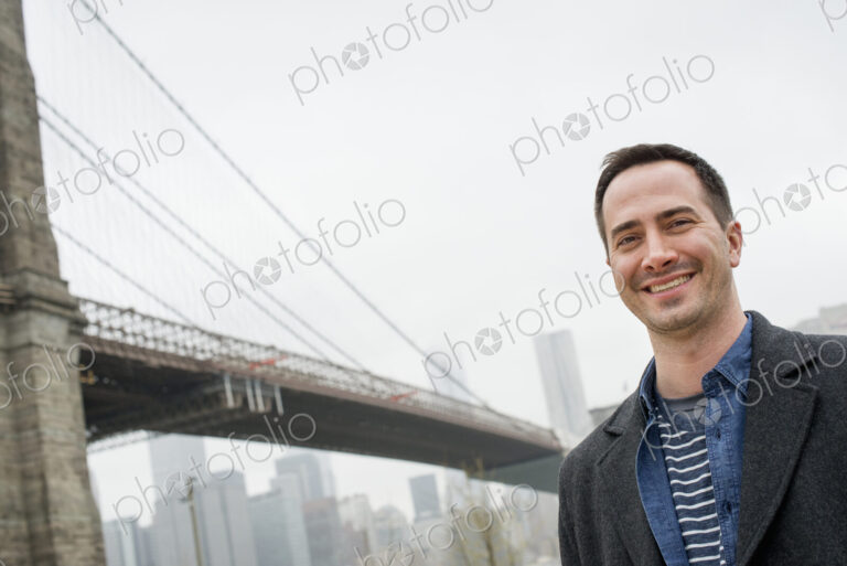 New York city, the Brooklyn Bridge crossing over the East River. A man wearing a grey…