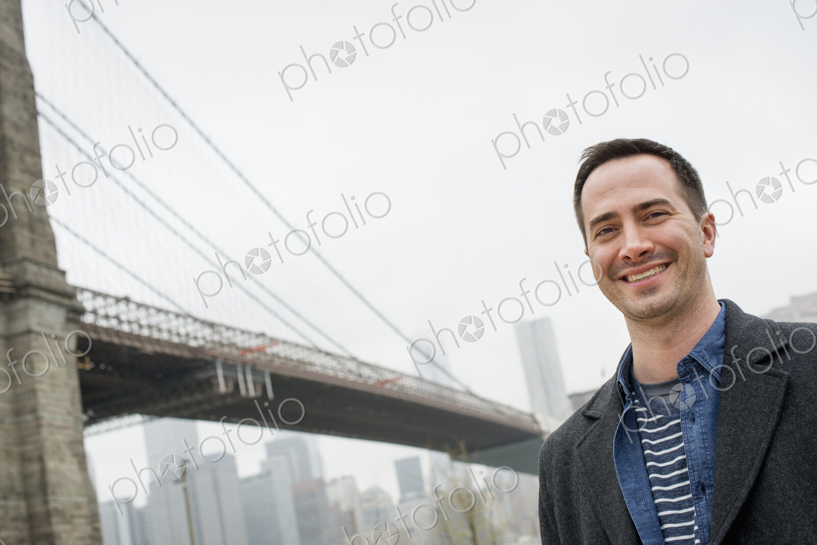 New York city, the Brooklyn Bridge crossing over the East River. A man wearing a grey…