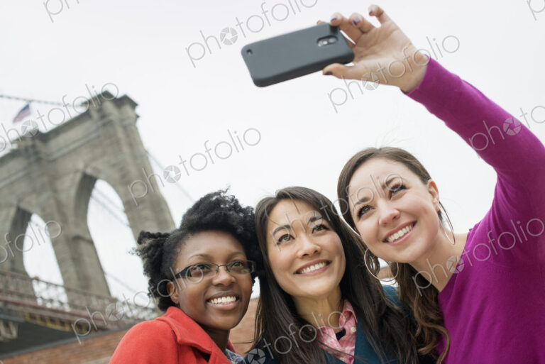 New York city, the Brooklyn Bridge crossing over the East River. Three women in a row,…