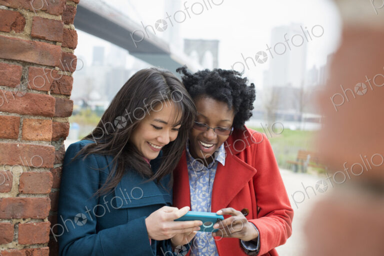 New York city, the Brooklyn Bridge crossing over the East River. Two women, side by…