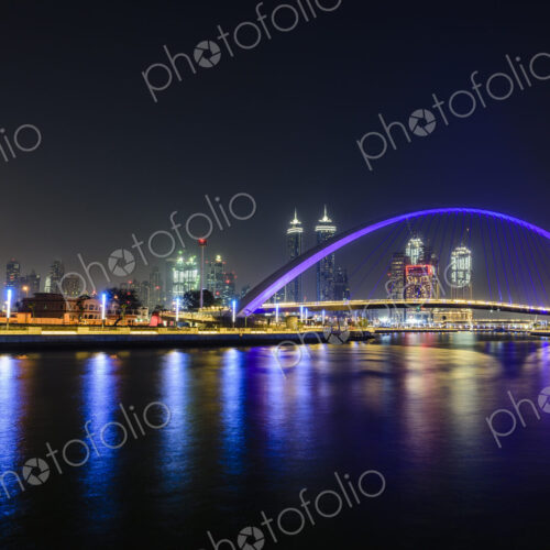 Night, cityscape of Dubai, tall buildings and waterfront, and arch over the creek.
