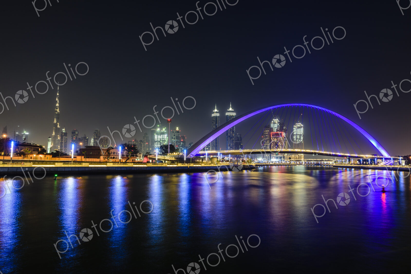 Night, cityscape of Dubai, tall buildings and waterfront, and arch over the creek.
