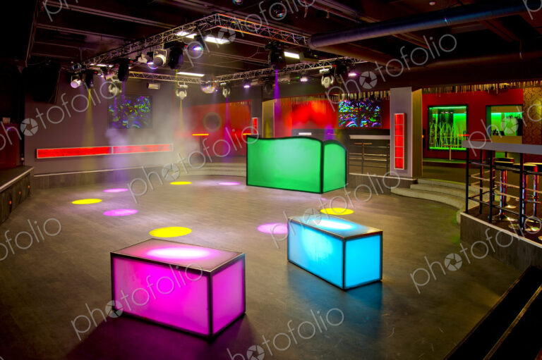 Nightclub interior, colourful lighting, wall screens and light boxes on a dance floor.