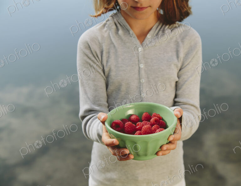 Nine year old girl holding bowl of organic raspberries