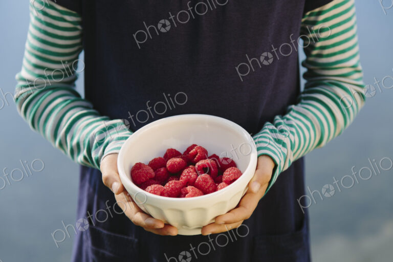 Nine year old girl holding bowl of organic raspberries