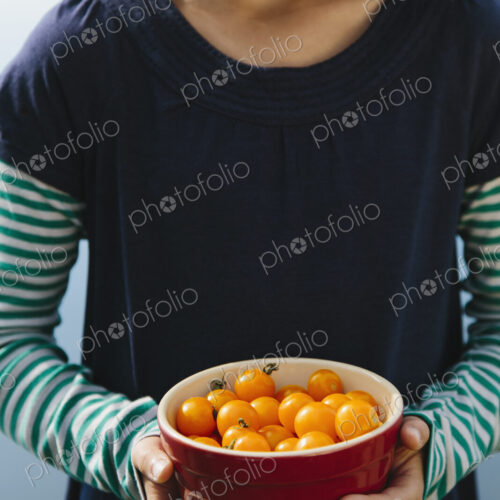 Nine year old girl holding bowl of organic yellow cherry tomatoes Nine year old girl holding bowl of organic yellow cherry tomatoes