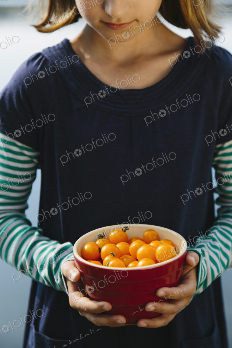 Nine year old girl holding bowl of organic yellow cherry tomatoes
