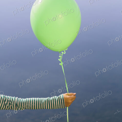 Nine year old girl holding green balloon, sitting by waters edge Nine year old girl holding green balloon, sitting by waters edge