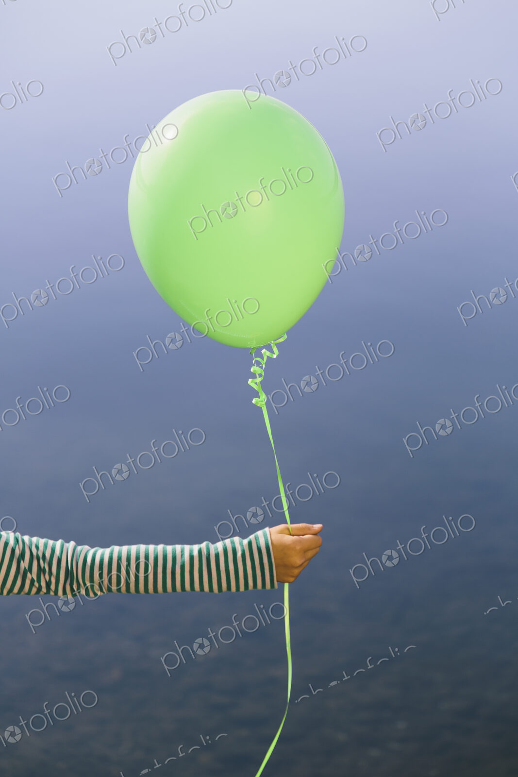 Nine year old girl holding green balloon, sitting by waters edge