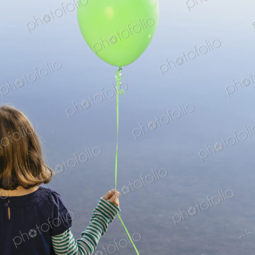 Nine year old girl holding green balloon, sitting by waters edge Nine year old girl holding green balloon, sitting by waters edge