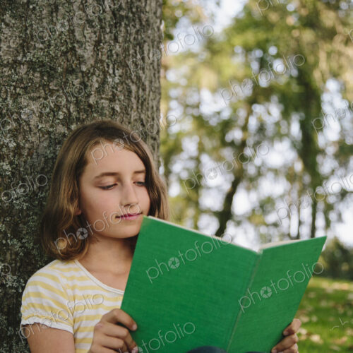 Nine year old girl sitting beneath tree, reading book Nine year old girl sitting beneath tree, reading book