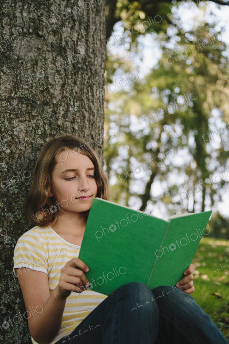Nine year old girl sitting beneath tree, reading book