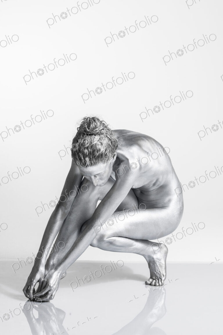 Nude Caucasian woman with silver body paint crouching
