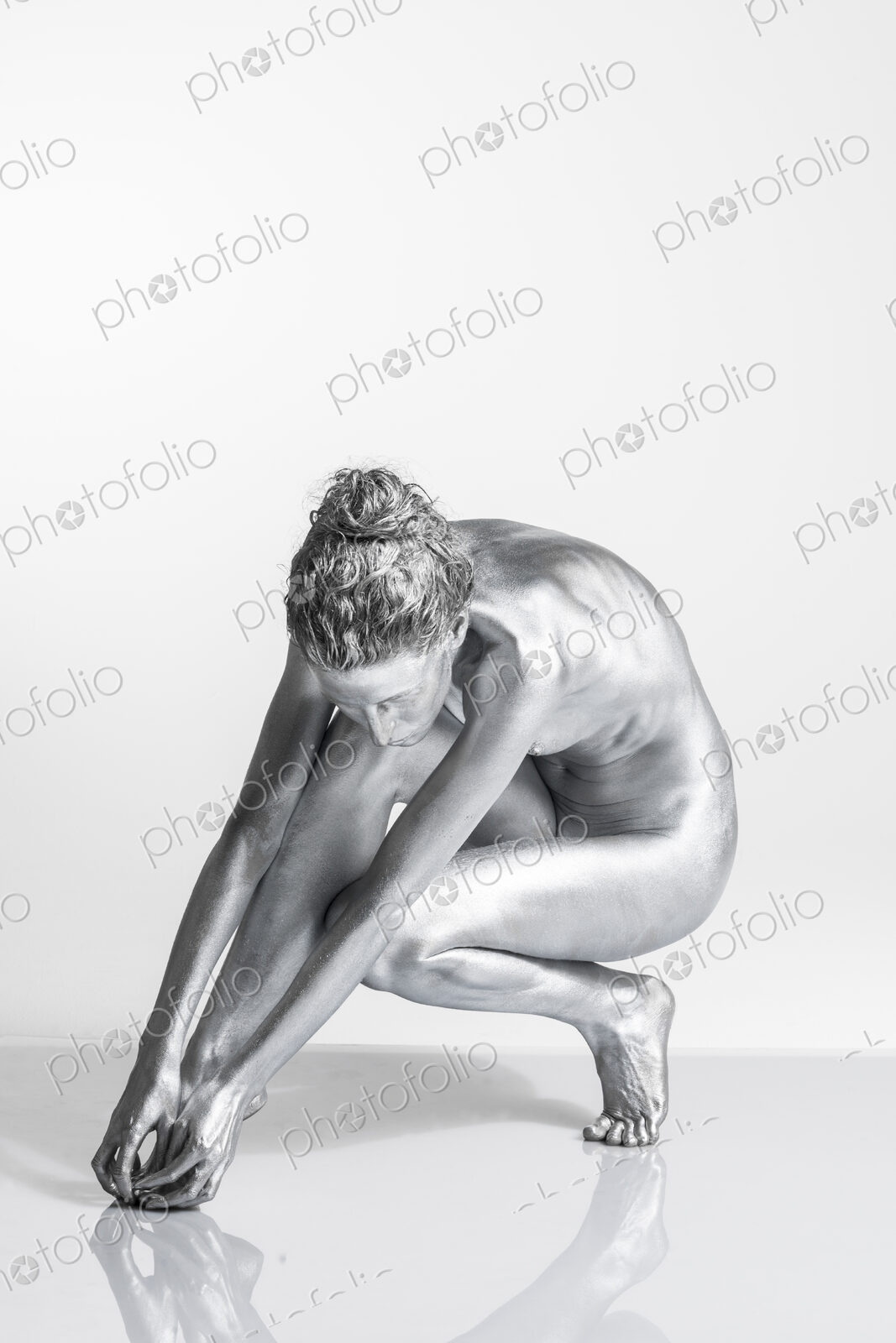 Nude Caucasian woman with silver body paint crouching