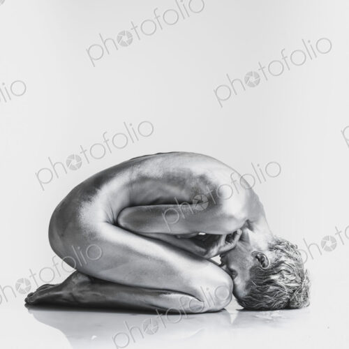 Nude Caucasian woman with silver body paint in fetal position Nude Caucasian woman with silver body paint in fetal position