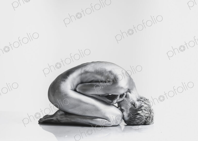 Nude Caucasian woman with silver body paint in fetal position