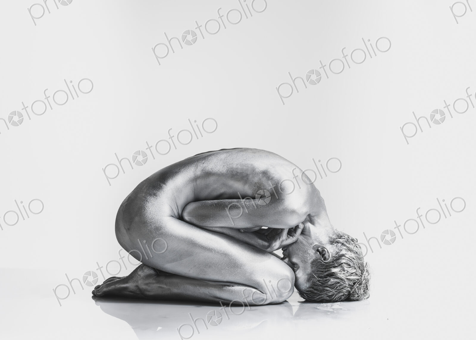 Nude Caucasian woman with silver body paint in fetal position