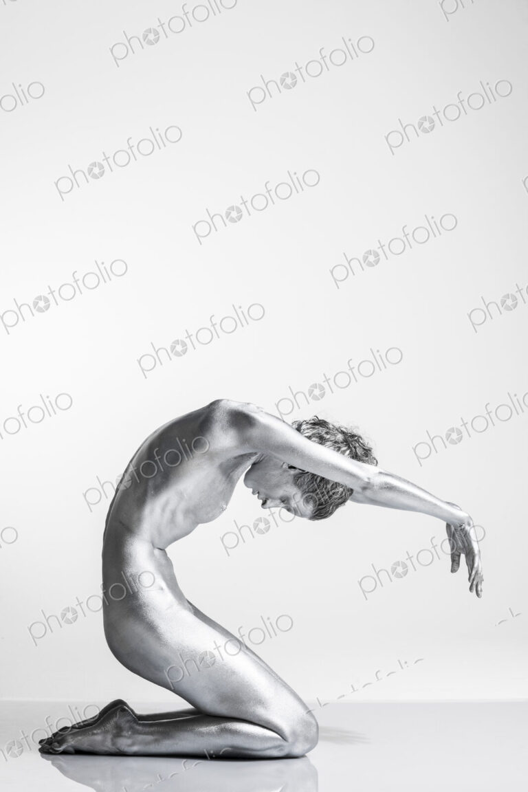 Nude Caucasian woman with silver body paint kneeling, arms forward and head bowed