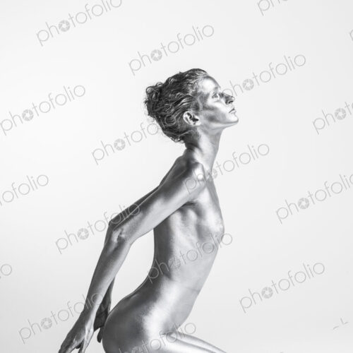 Nude Caucasian woman with silver body paint kneeling, hands behind her Nude Caucasian woman with silver body paint kneeling, hands behind her