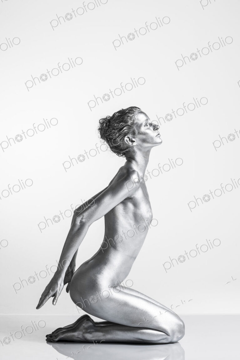 Nude Caucasian woman with silver body paint kneeling, hands behind her